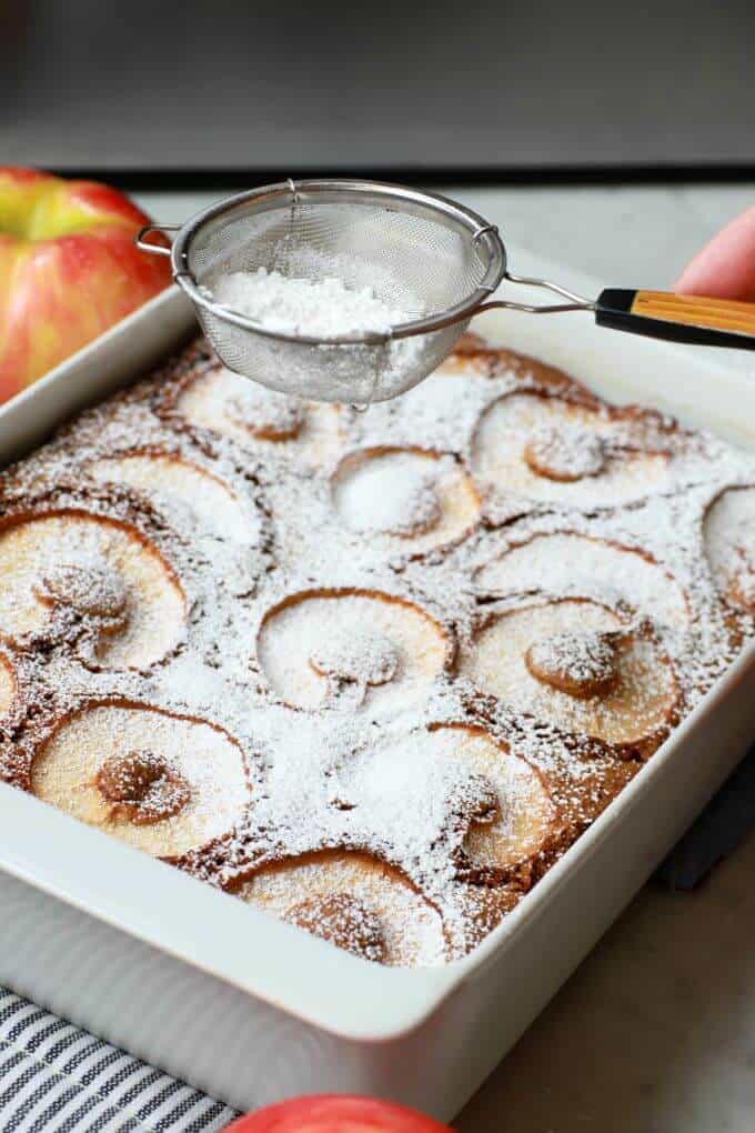 A small strainer dusts powdered sugar onto a cake.