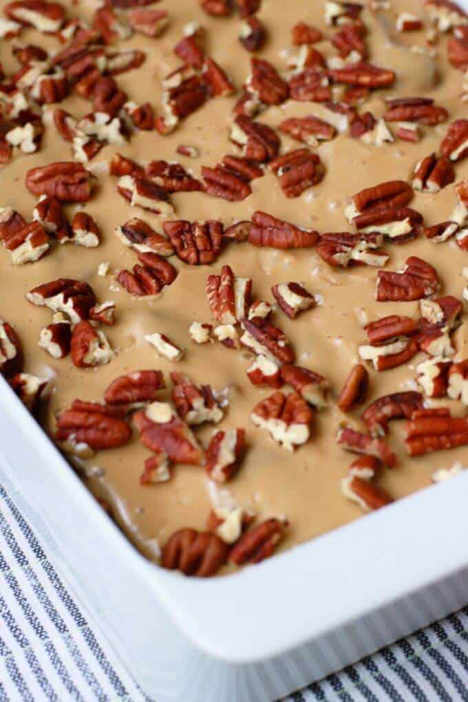 A white baking pan holds a golden baked Apple Dapple Cake topped with brown butter glaze and pecans.