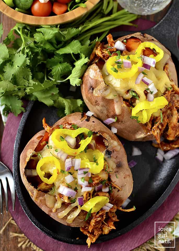 These 25 Awesome Stuffed Baked Potato Recipes are pure comfort food but some are very healthy too! These stuffed potatoes can easily be an entire meal. #stuffedbakedpotato #bakedsweetpotato #bakedpotatomeal BBQ Chicken stuffed sweet potatoes on a black skillet with a bunch of parsly and a fork