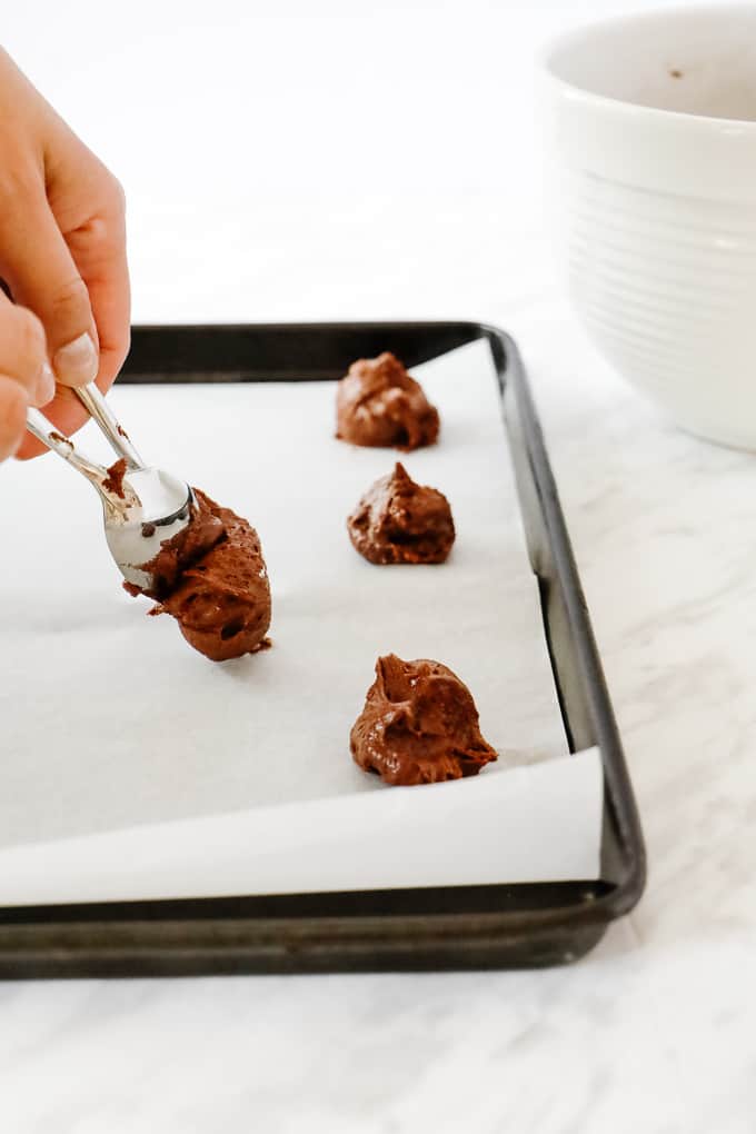 Dropping spoonfuls of chocolate cookies onto a parchment lined cookie sheet