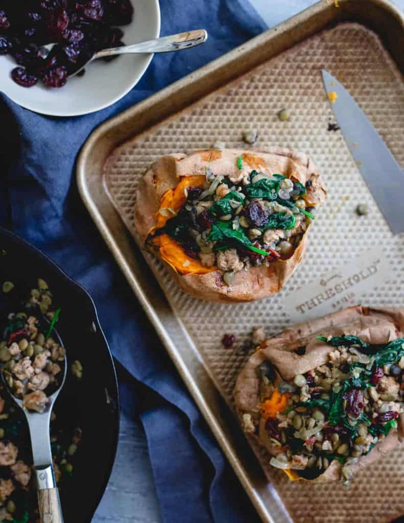 Turkey Sausage Stuffed Sweet Potatoes With Tart Cherries and Lentils on a baking tray with small bowl of tart cherries and ground turkey sausage beside it