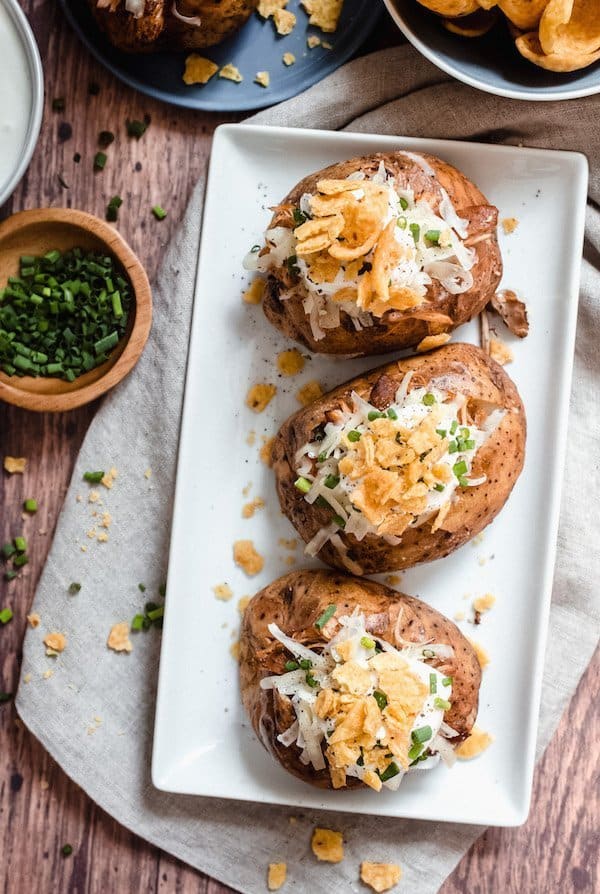 Chicken Taco Loaded Baked Potatoes on a white platters with a bowl of chopped chives beside