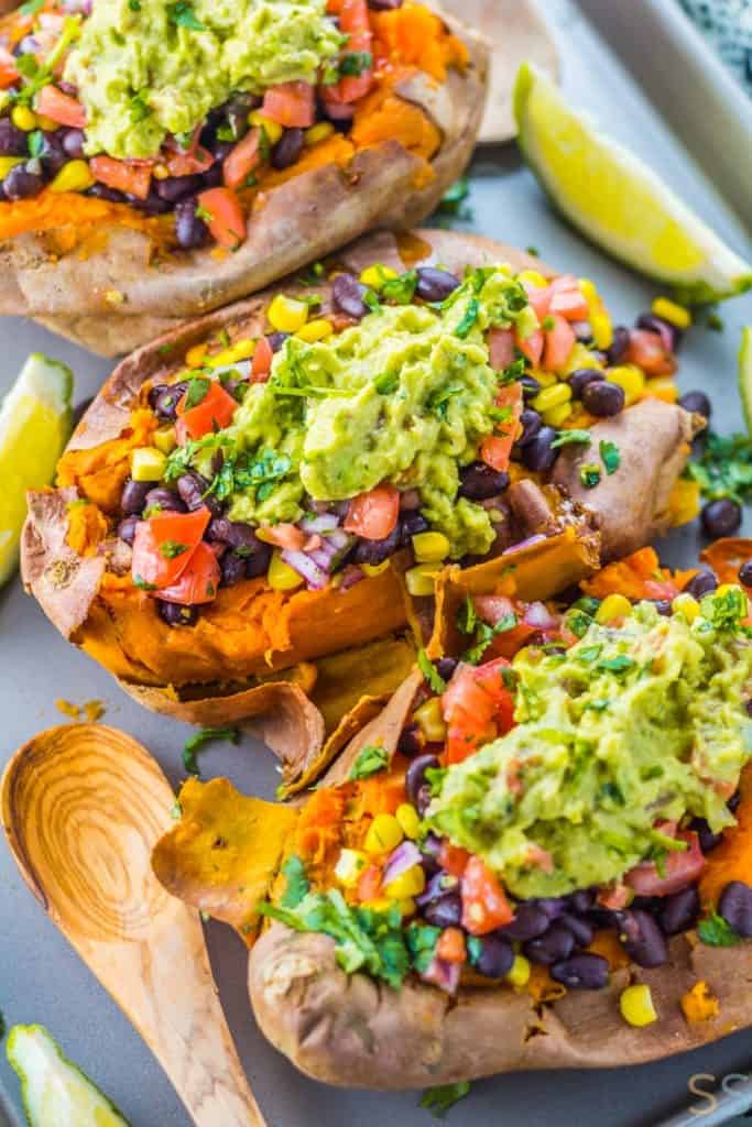 Black bean taco stuffed sweet potatoes on a cooking tray with a wooden spoon and lime wedges