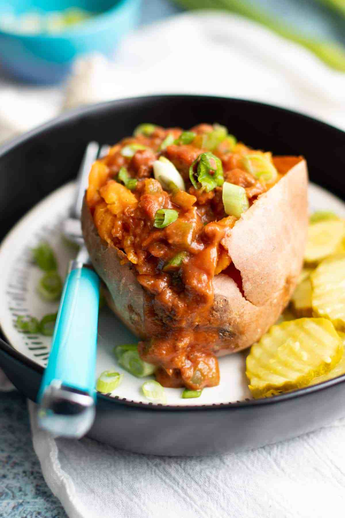 Sloppy Joes Stuffed Sweet Potatoeon a plate with a fork and some sliced pickles.