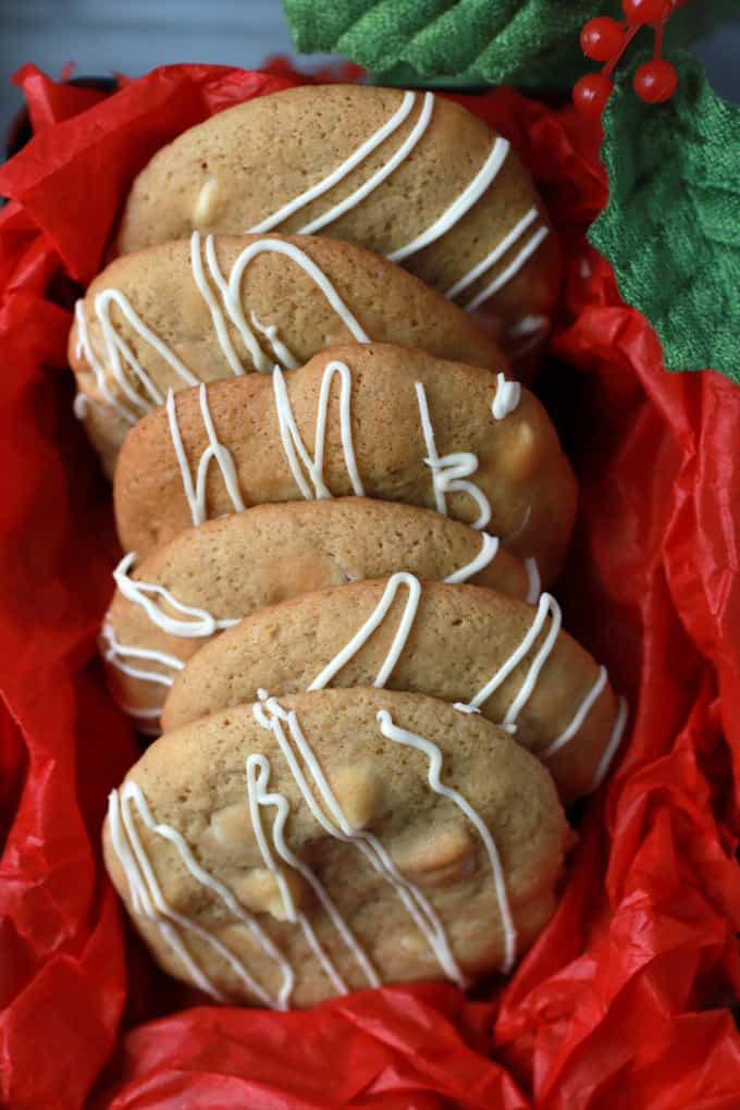 Golden baked cookies with white drizzle in a red tissue paper lined cookie tin.