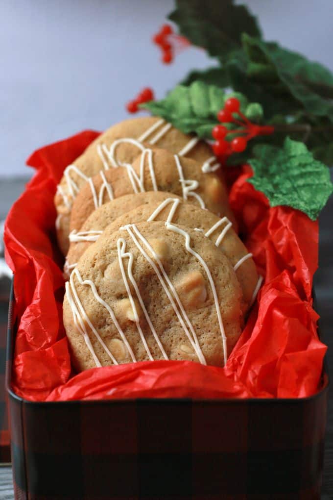 Golden baked cookies with white drizzle in a red tissue paper lined cookie tin.