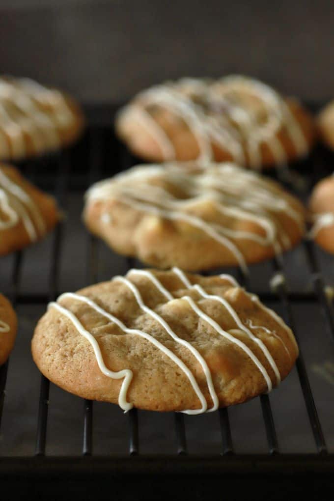 Golden baked cookies drizzled with white chocolate on a black cookie rack.