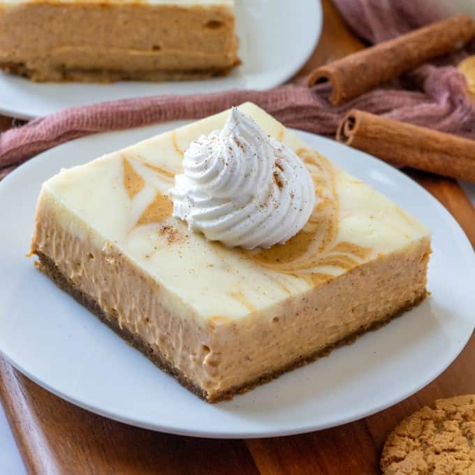 Closeup of pumpkin cheesecake bars with whipped cream on top. 