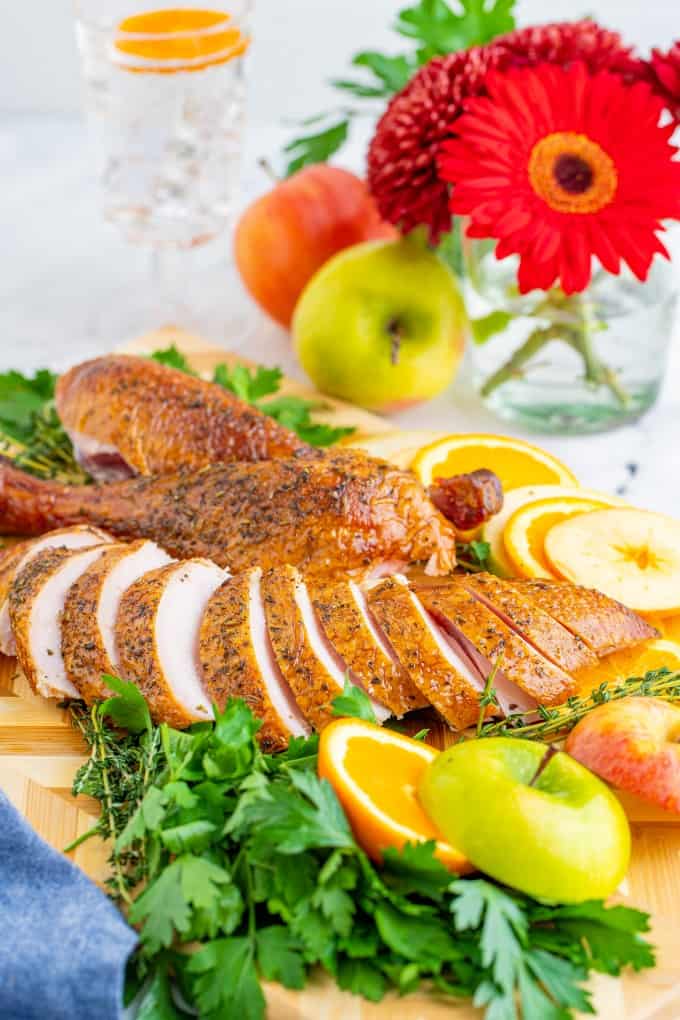 Sliced turkey on a board with sliced apples and oranges and herbs