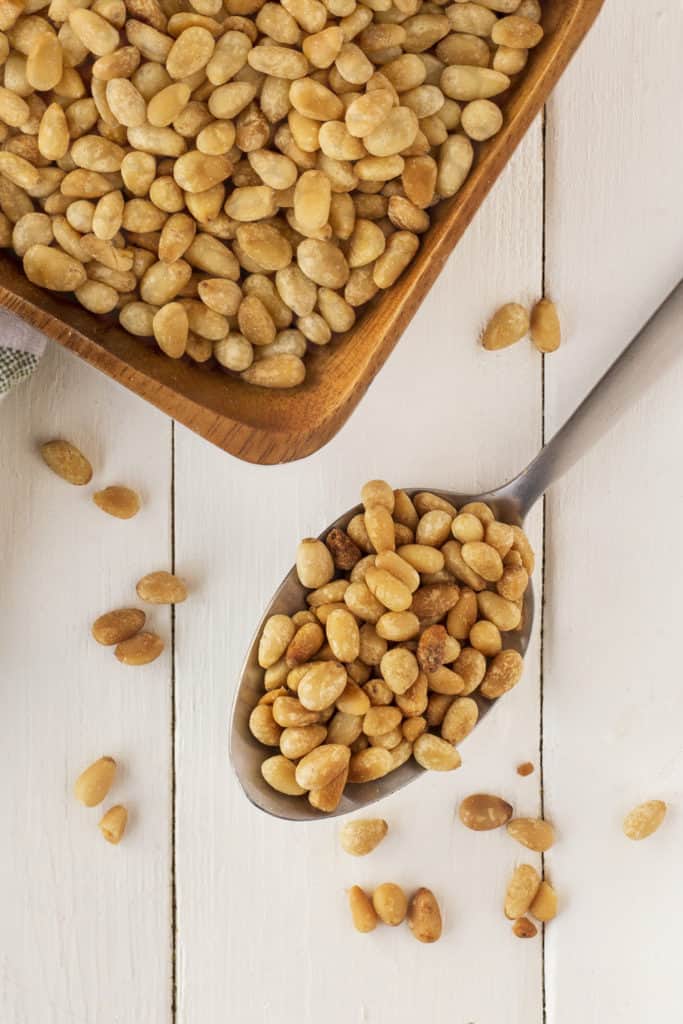 Spoon full of toasted pine nuts and also in a bowl