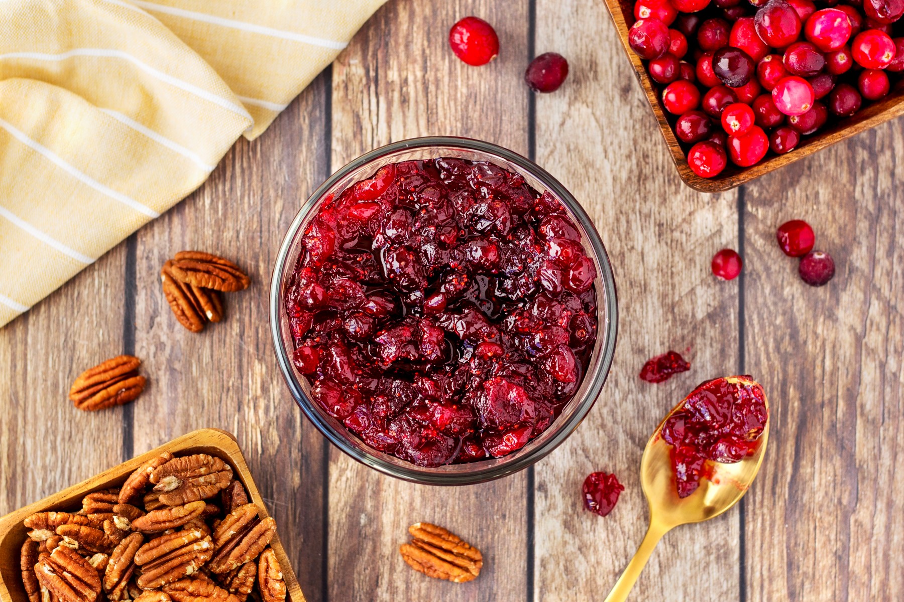 Horizontal shot of cranberry sauce in a bowl with fresh cranberries and pecans around and in a containers. 