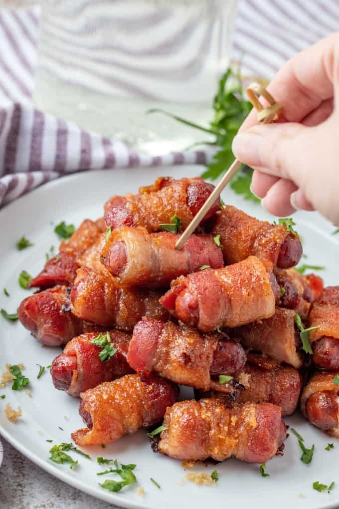 Sticking a cocktail skewer into a plateful of bacon wrapped smokies. 