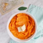 Top view of a butternut squash mash with 2 squares of butter, sage leaves on the side