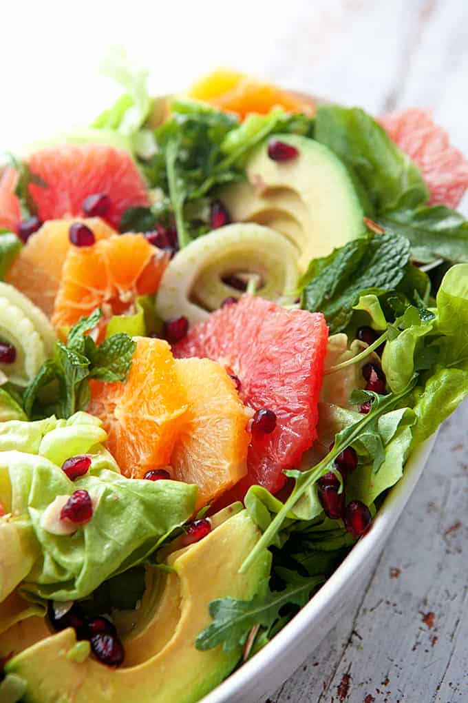 Close up of a greens, oranges, grapefruits, avocado and pomegranate seeds in a bowl. 