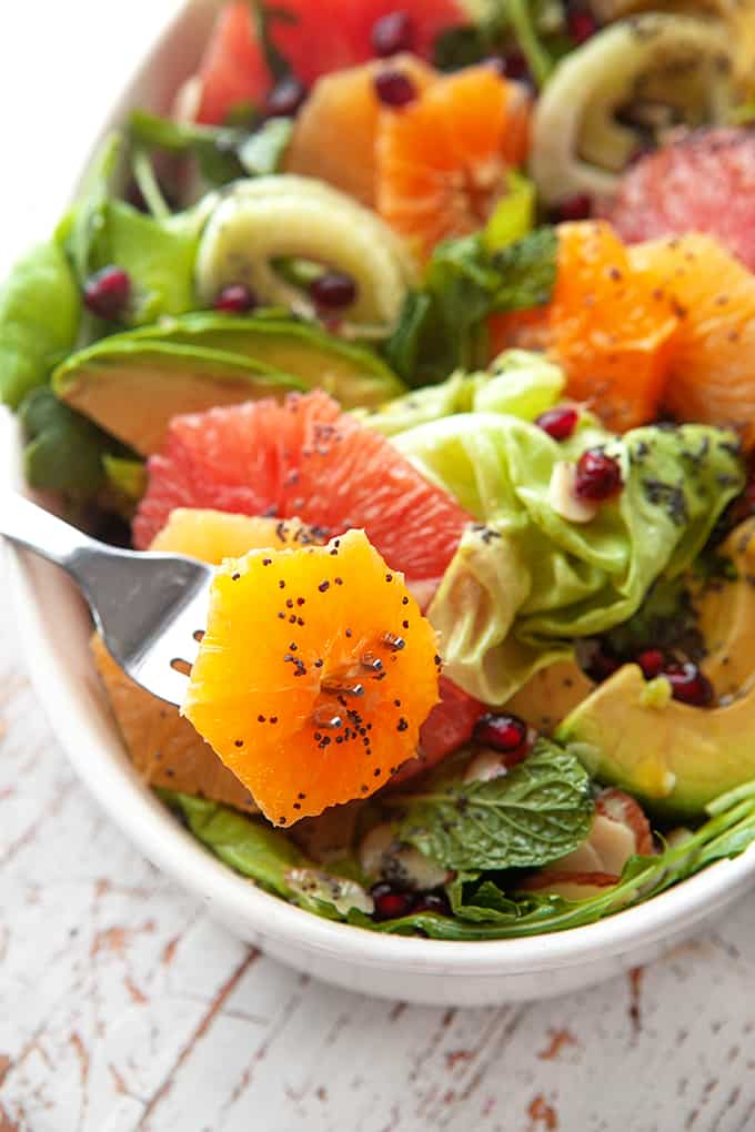 Grabbing an orange with a fork from a large platter of salad. 