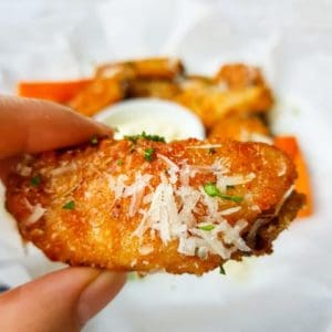 Baked Garlic Parmesan Chicken Wings in a hand over a patter of wings