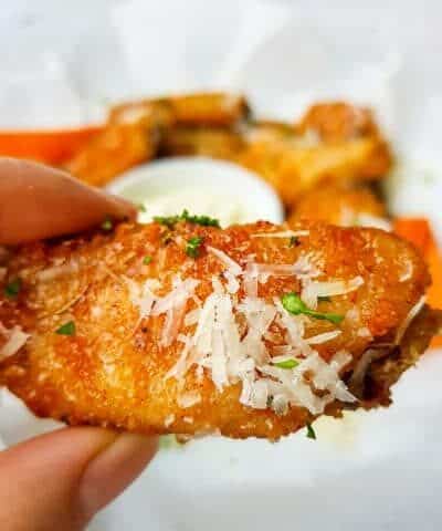 Baked Garlic Parmesan Chicken Wings in a hand over a patter of wings