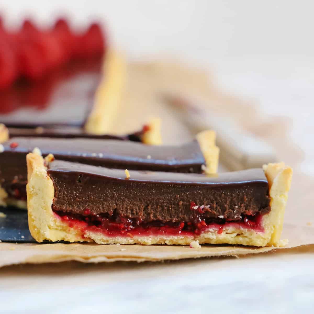 Square photo of a close up of a sliced chocolate tart with raspberry jam.