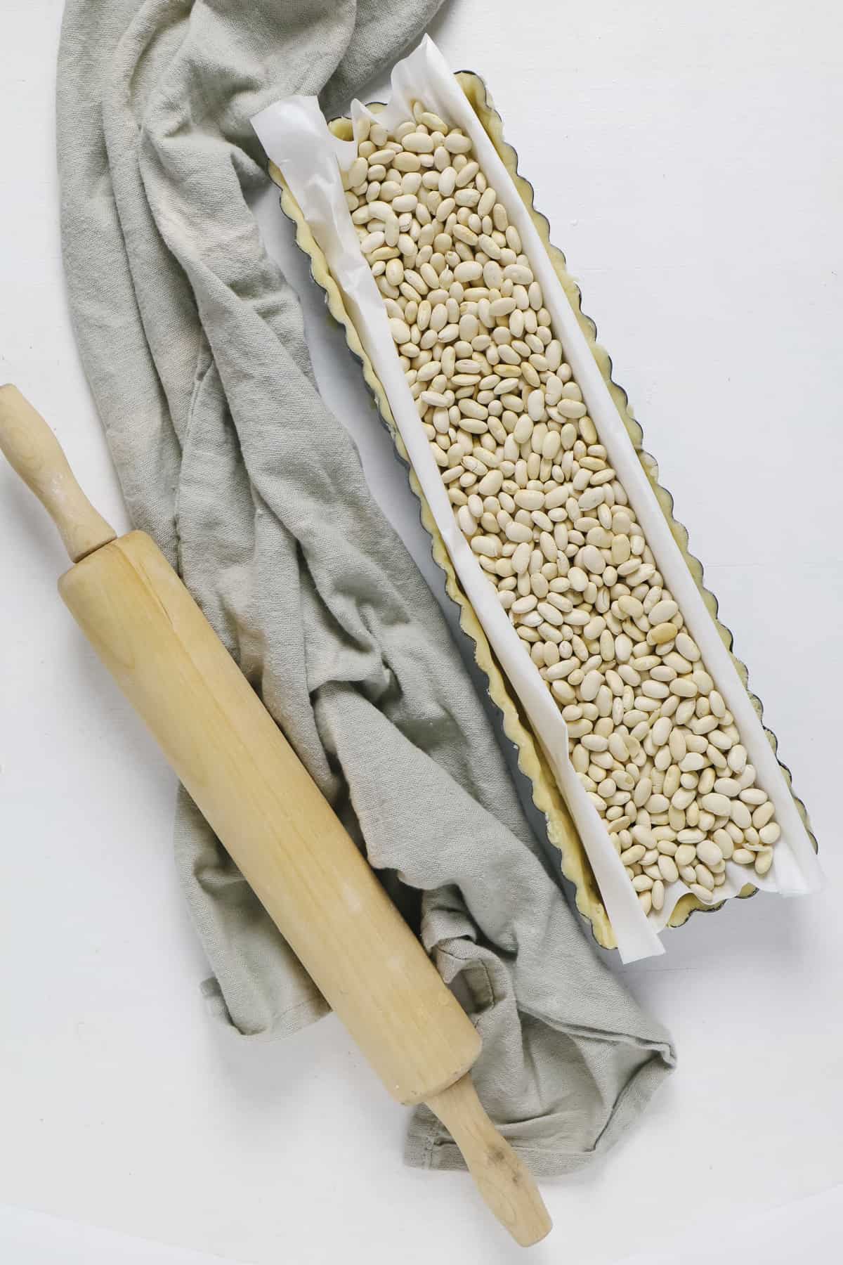 Top view of a dish filled with dry beans and a rolling pin beside it. 