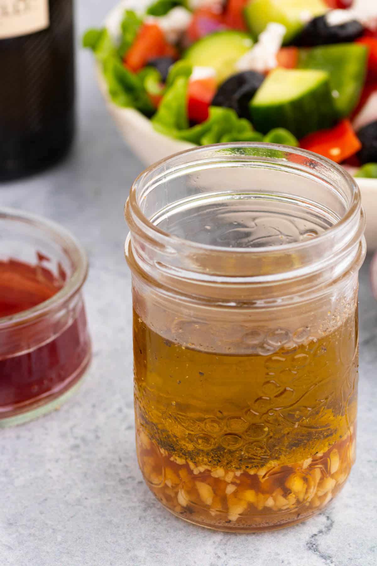 A glass jar containing layers of red wine vinaigrette dressing ingredients.