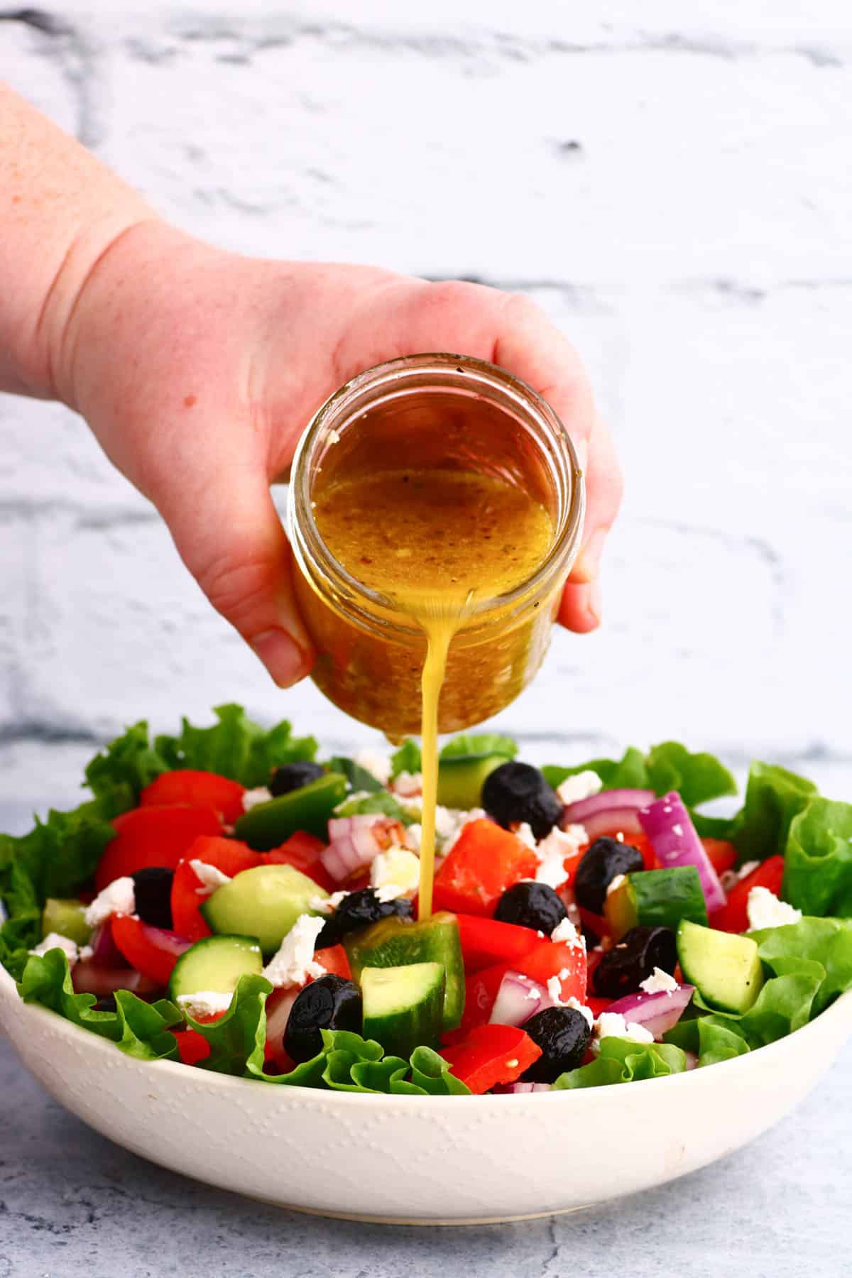 Salad dressing being poured on a bright chopped salad.