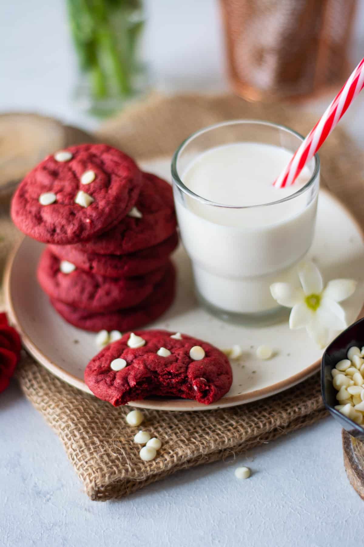 Red velvet cookies on a plate with a glass of milk, one with a bite taken out. 
