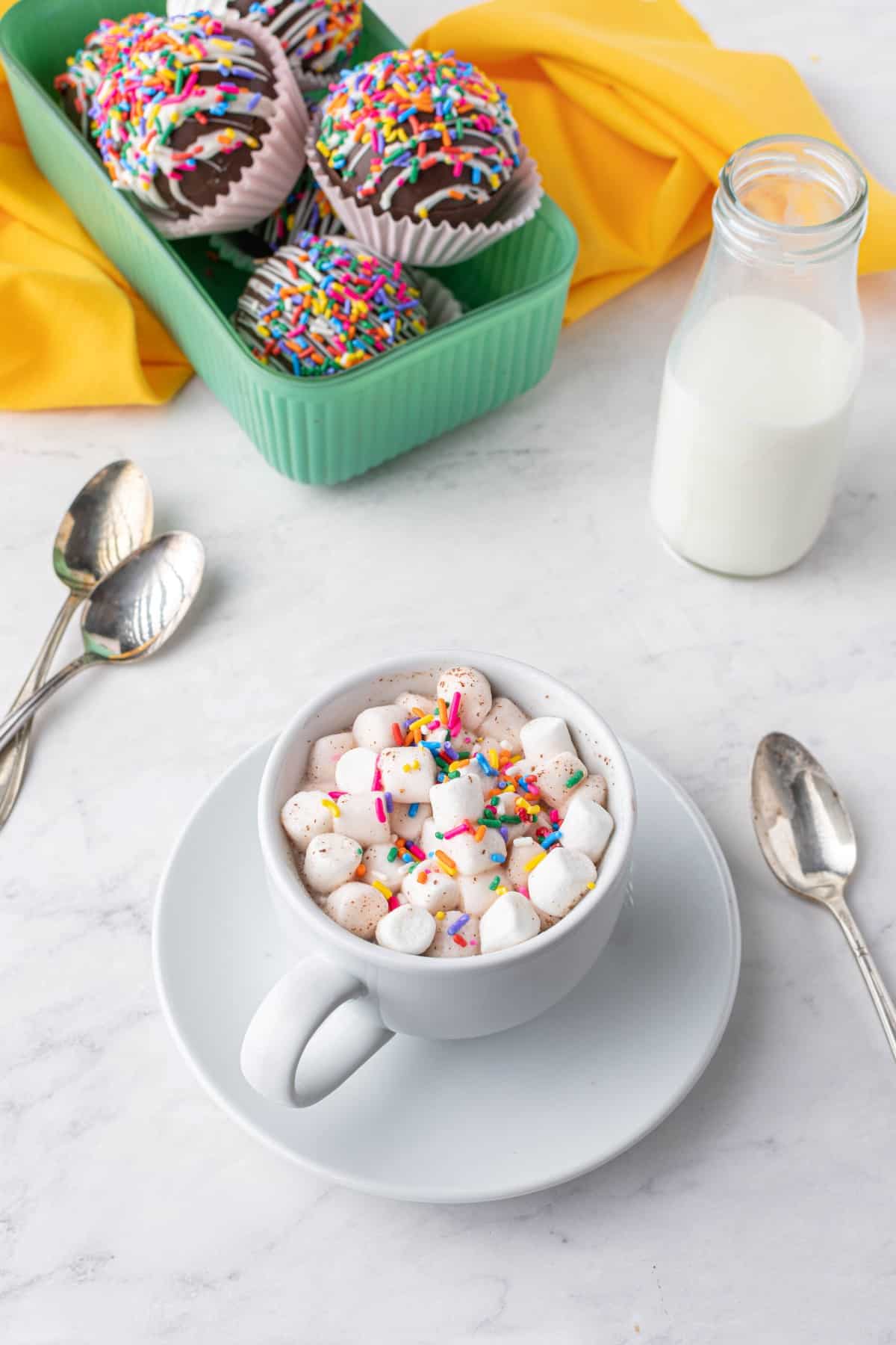 Cup of hot chocolate in a white mug and saucer with lots of mini marshmallows and sprinkles.