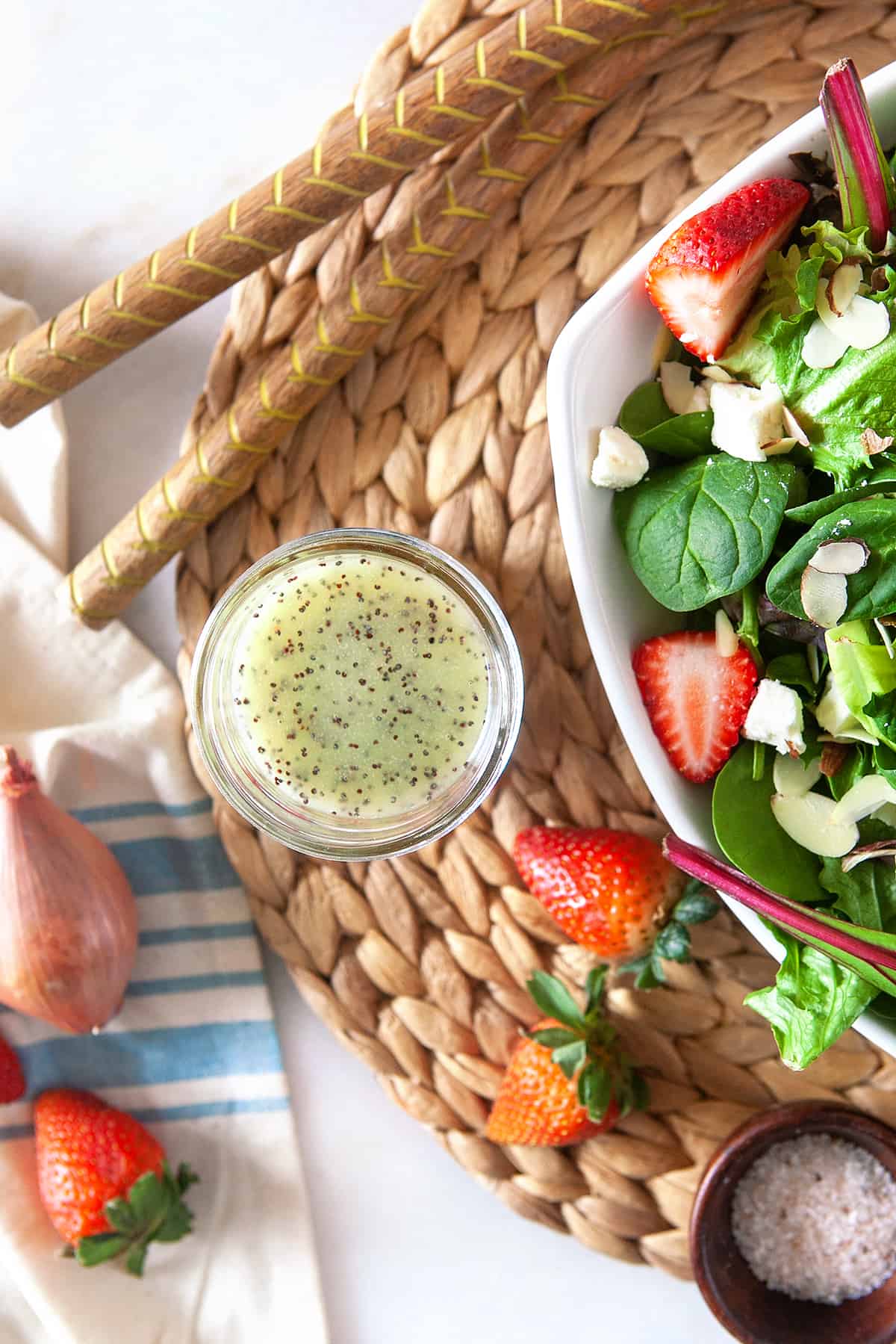 Overhead of homemade poppy seed dressing in a jar on a woven mat with a strawberry salad. 