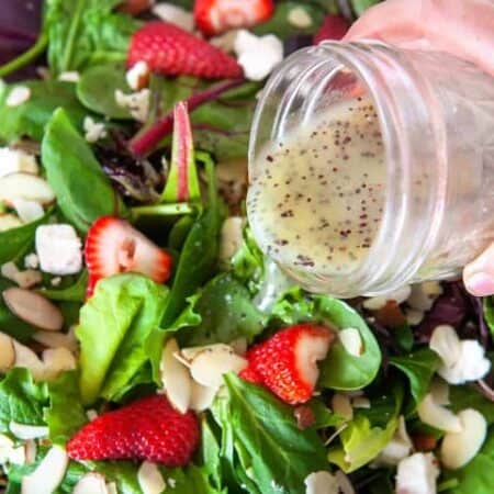 Poppy Seed Dressing being poured from a mason jar over a mixed green salad