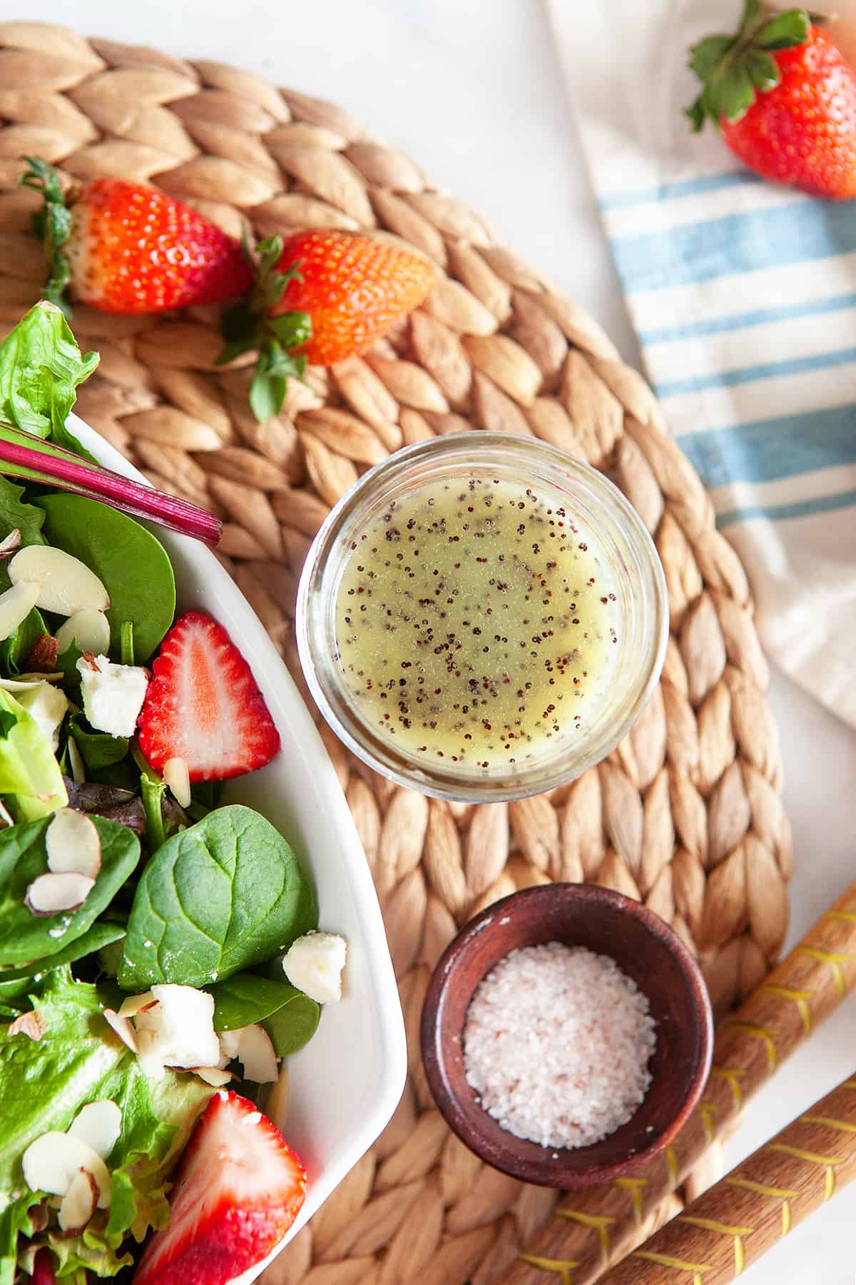Overhead of poppy seed dressing with a bowl of salt and a strawberry salad