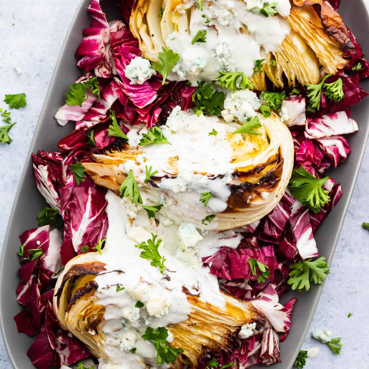 A platter holds roasted cabbage wedges topped with chunky blue cheese sauce all sitting on a bed of purple radicchio. 