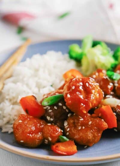 Sweet and sour pork on a plate with rice and veggies.