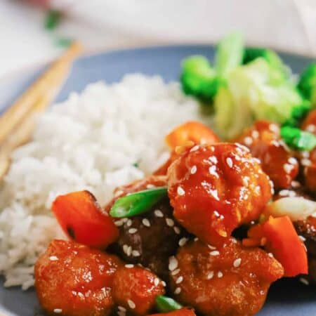 Sweet and sour pork on a plate with rice and veggies.