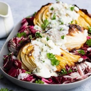 A platter holds roasted cabbage wedges topped with chunky blue cheese sauce all sitting on a bed of purple radicchio.