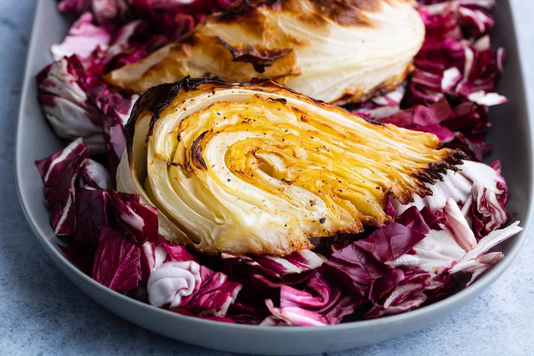 A platter holds a wedge of roasted cabbage on a bed of purple radicchio. 