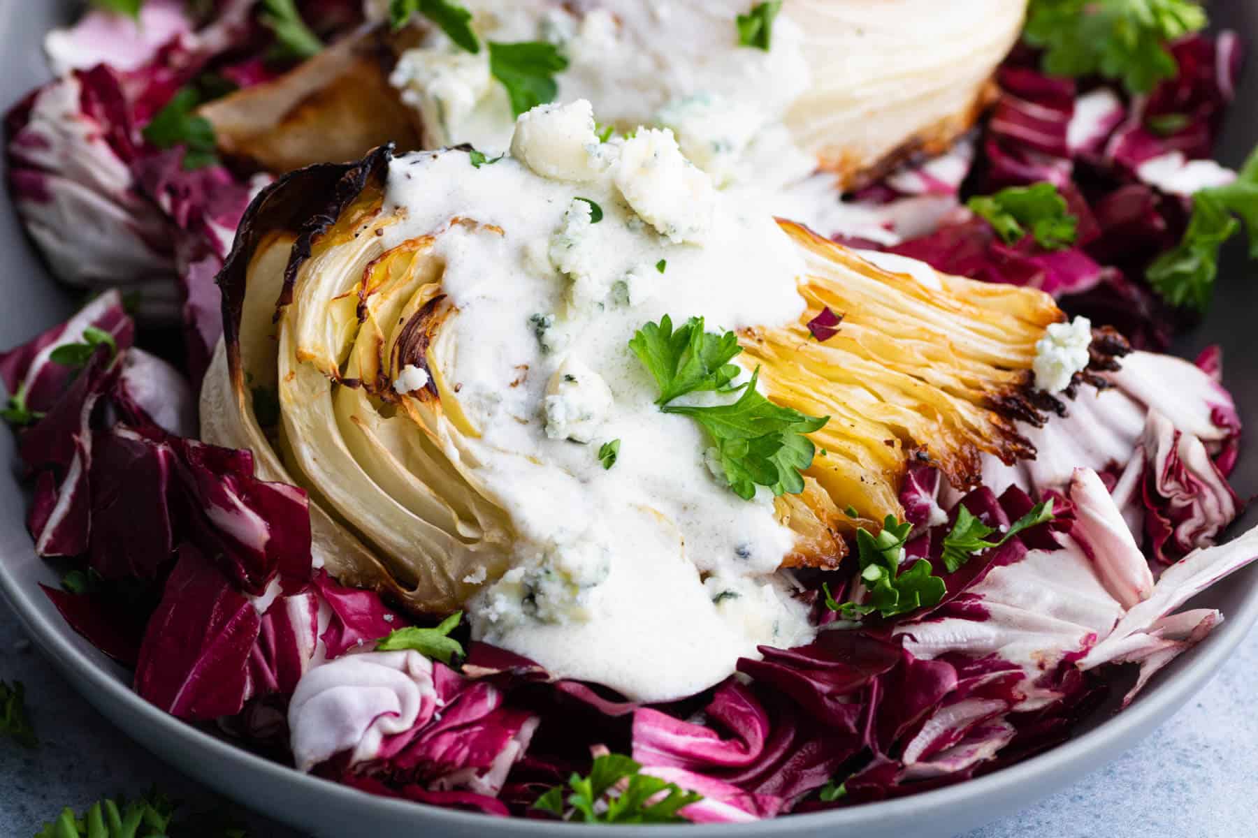 A platter holds roasted cabbage wedges topped with chunky blue cheese sauce all sitting on a bed of purple radicchio.