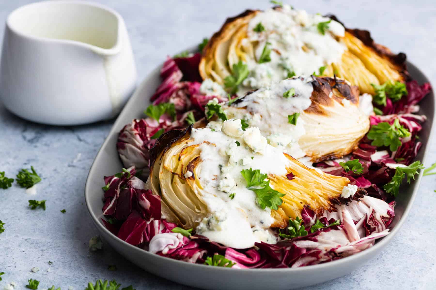 A platter holds roasted cabbage wedges topped with chunky blue cheese sauce all sitting on a bed of purple radicchio.