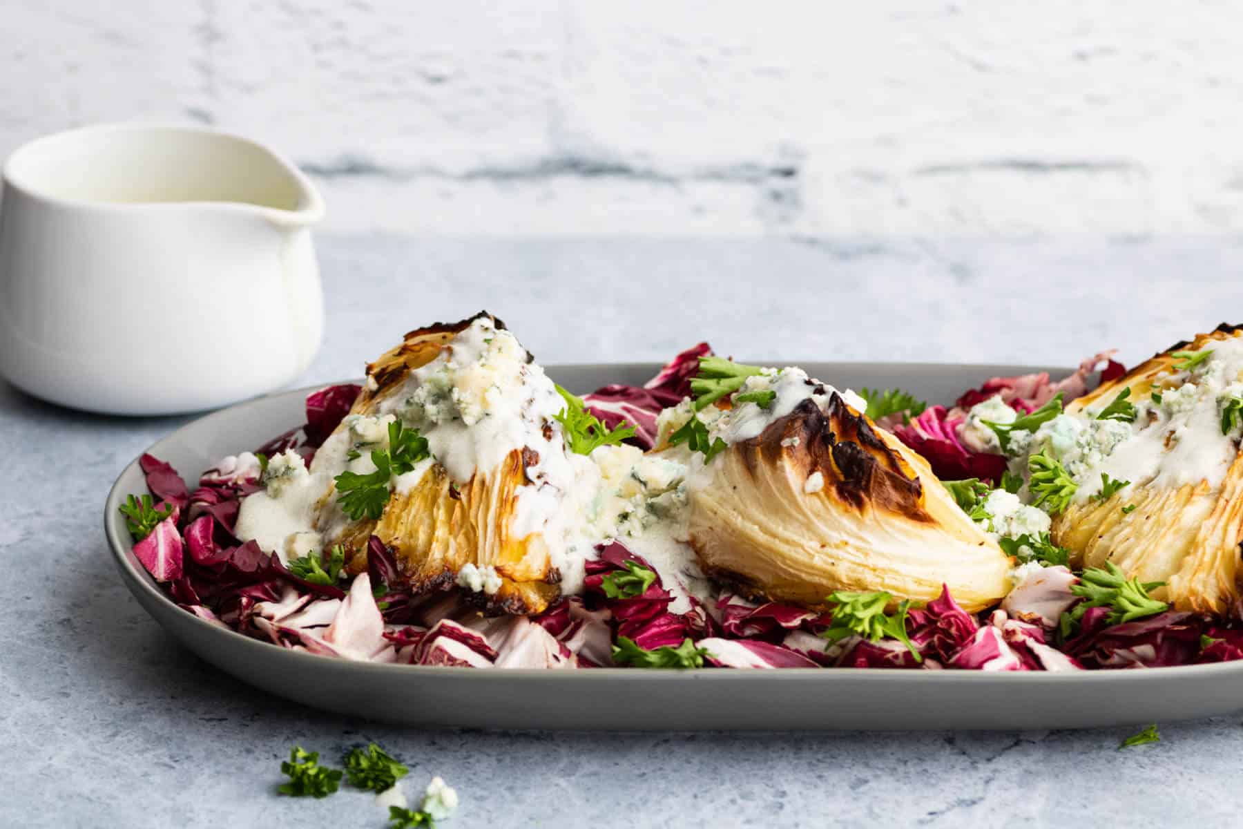 A platter holds roasted cabbage wedges topped with chunky blue cheese sauce all sitting on a bed of purple radicchio.