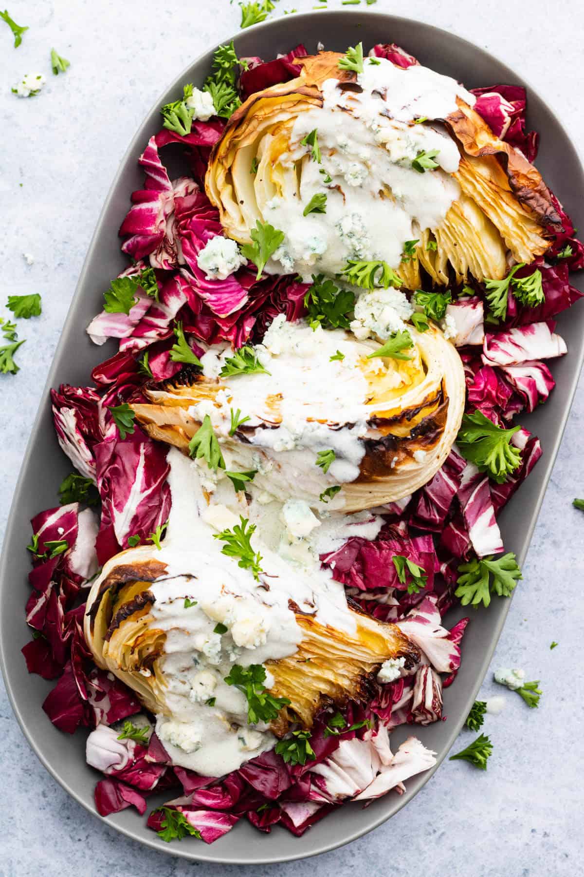 A platter holds roasted cabbage wedges topped with chunky blue cheese sauce all sitting on a bed of purple radicchio. 