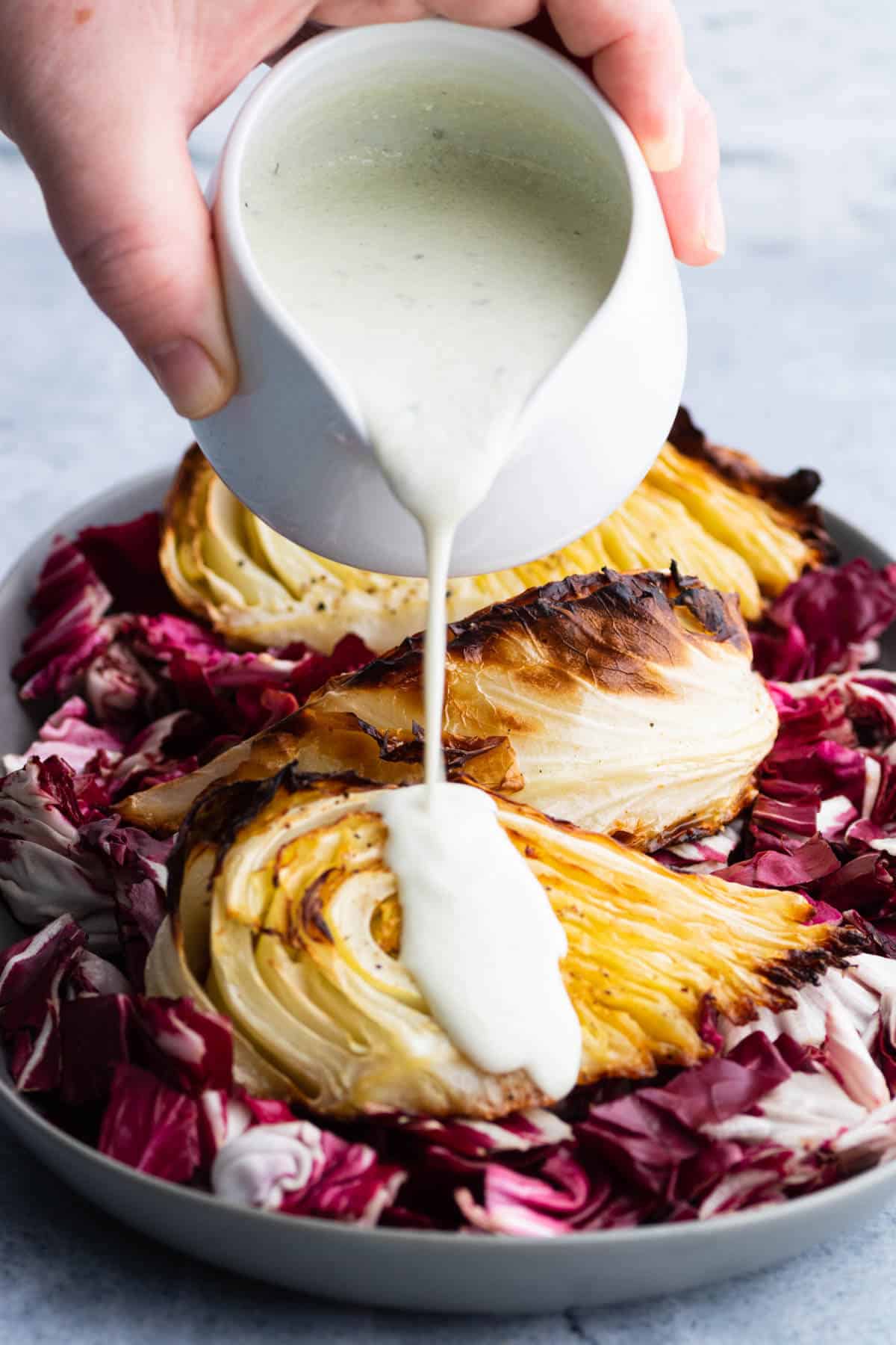 A creamy sauce being poured over roasted cabbage wedges.