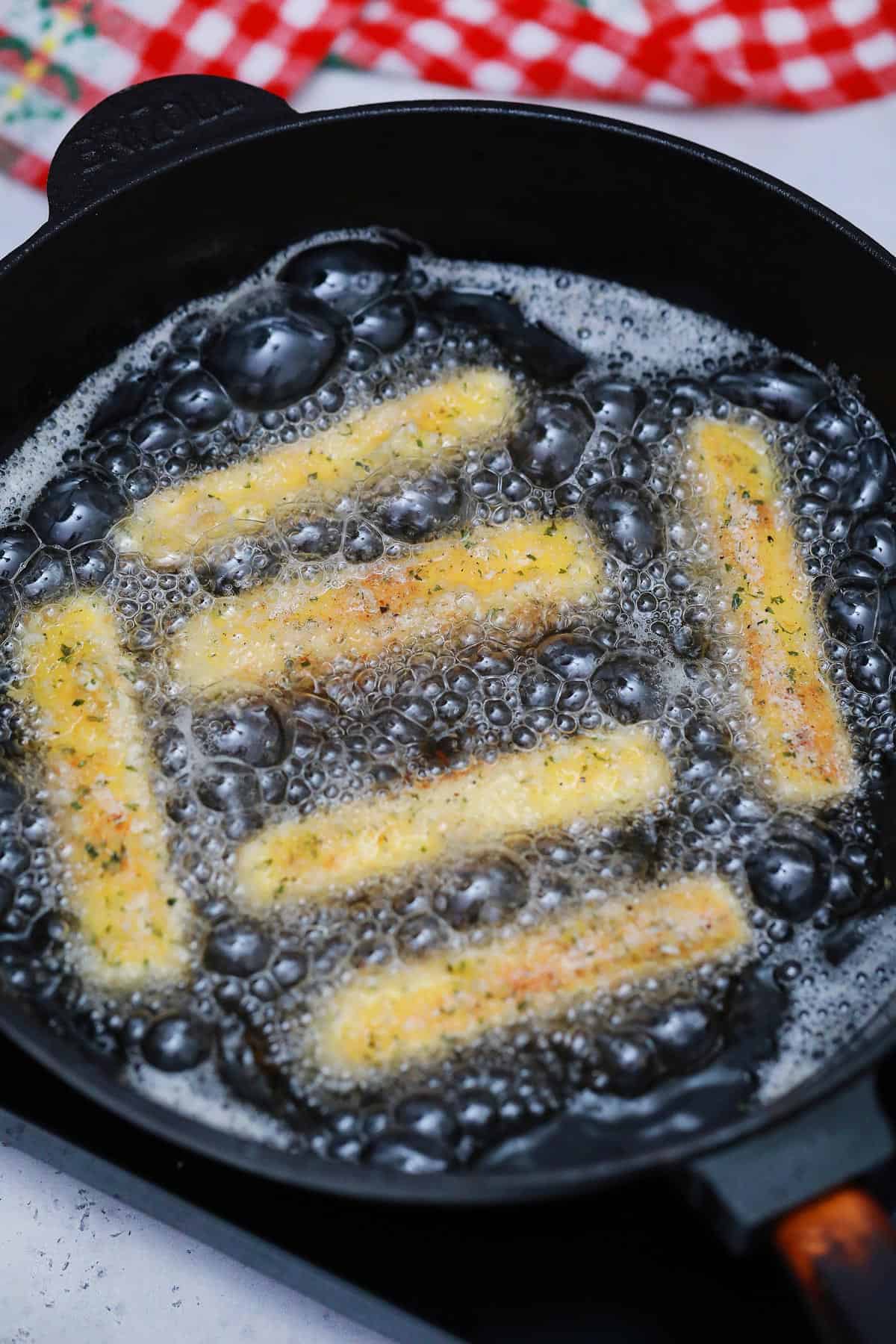 Cheese sticks in a cast iron pan frying. 