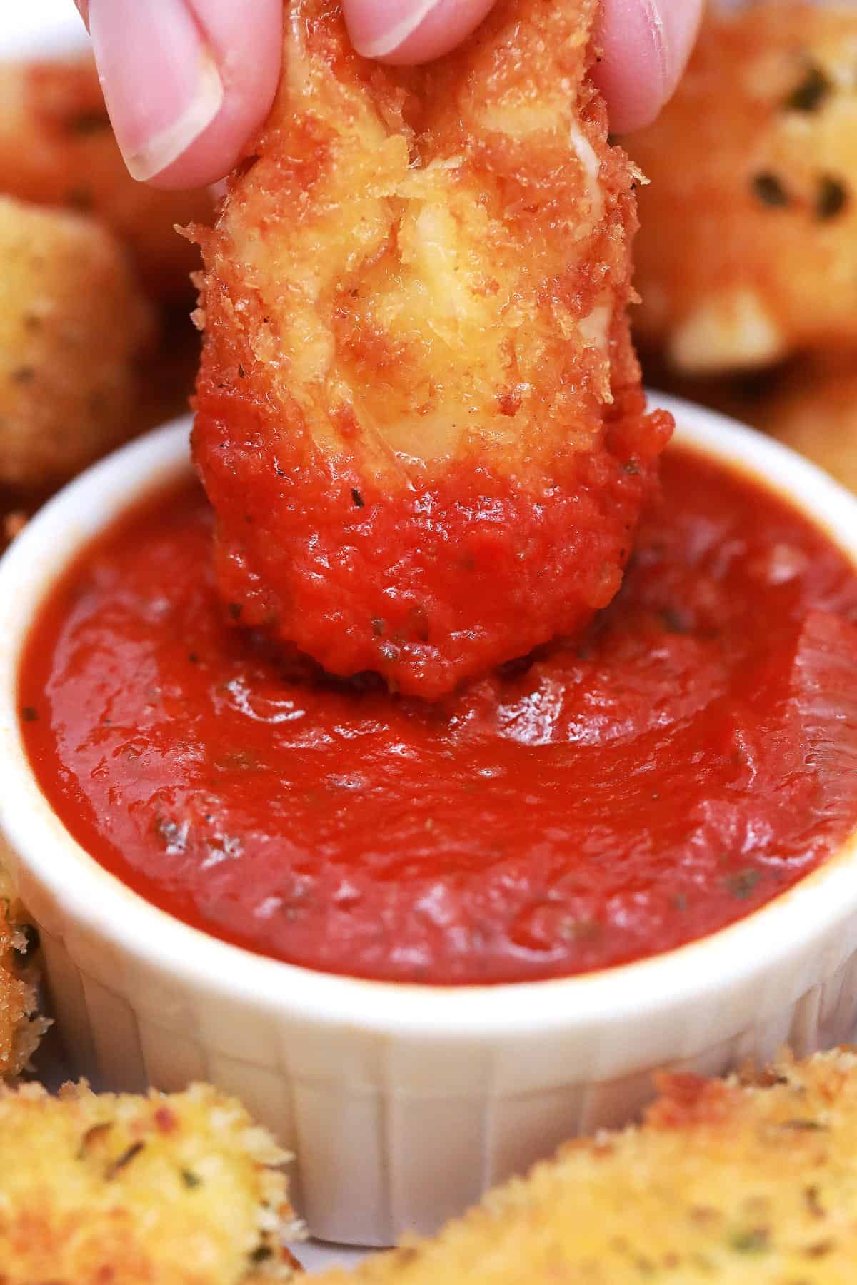 Close up of a cheese stick being dipped in marinara sauce