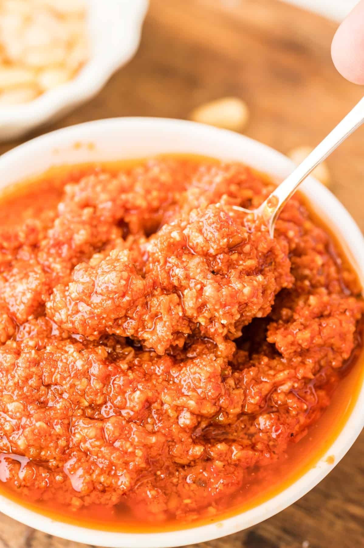Close up of red pesto in a bowl with a spoon. 
