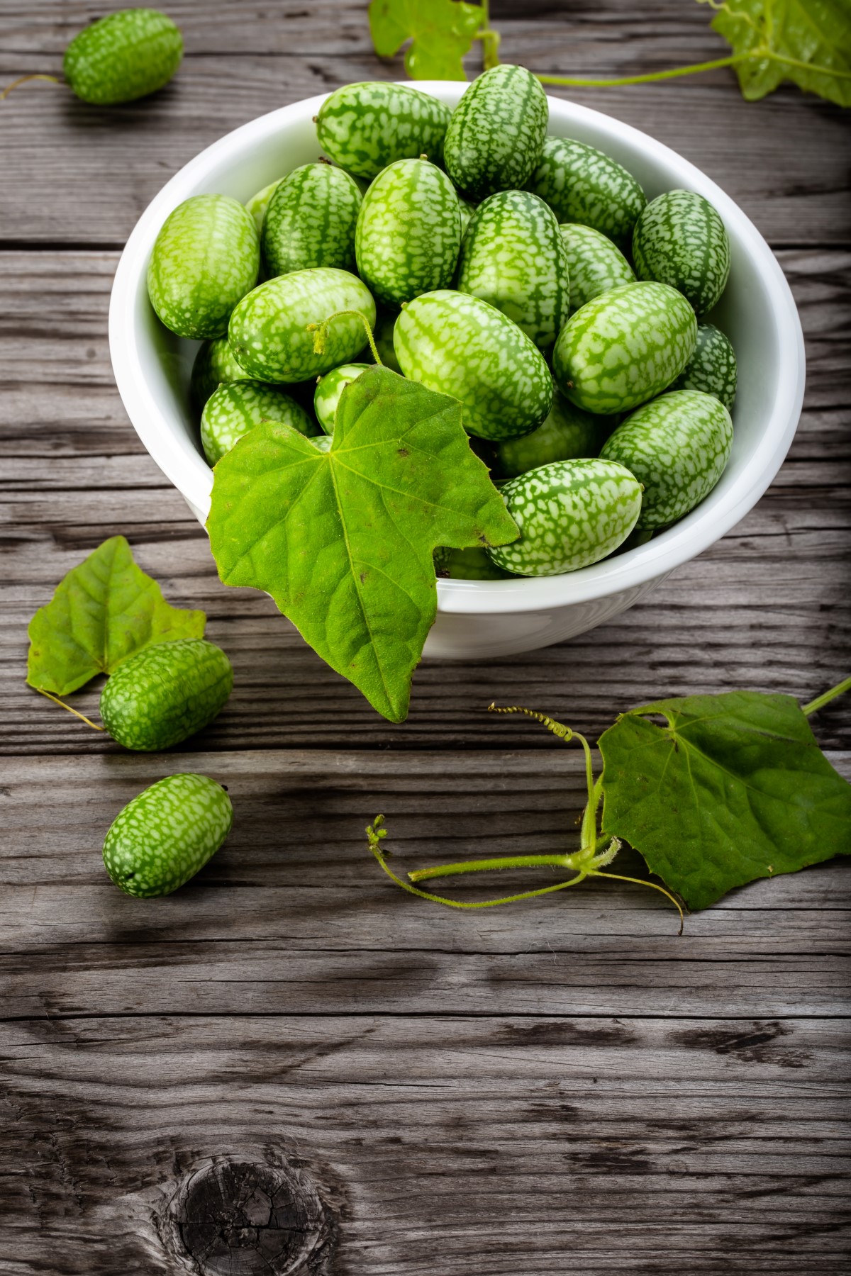 Bowl of cucamelons in plate on rustic table vertical