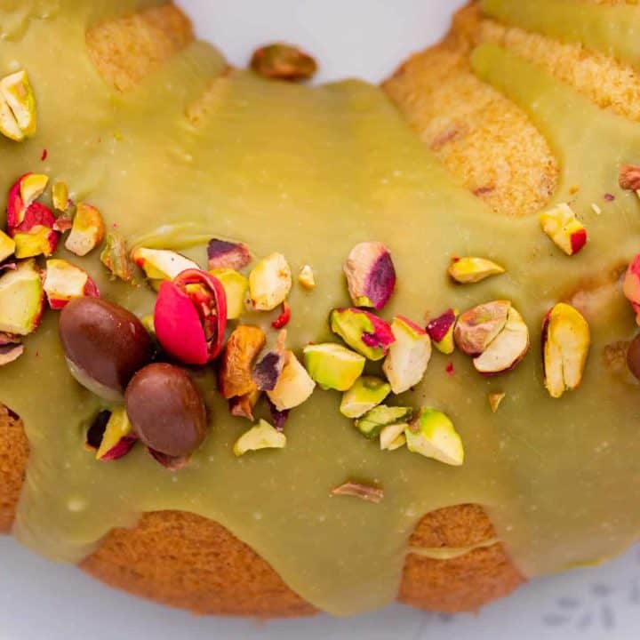 Close up of a green glazed bundt cake decorated with chopped and whole pistachios.