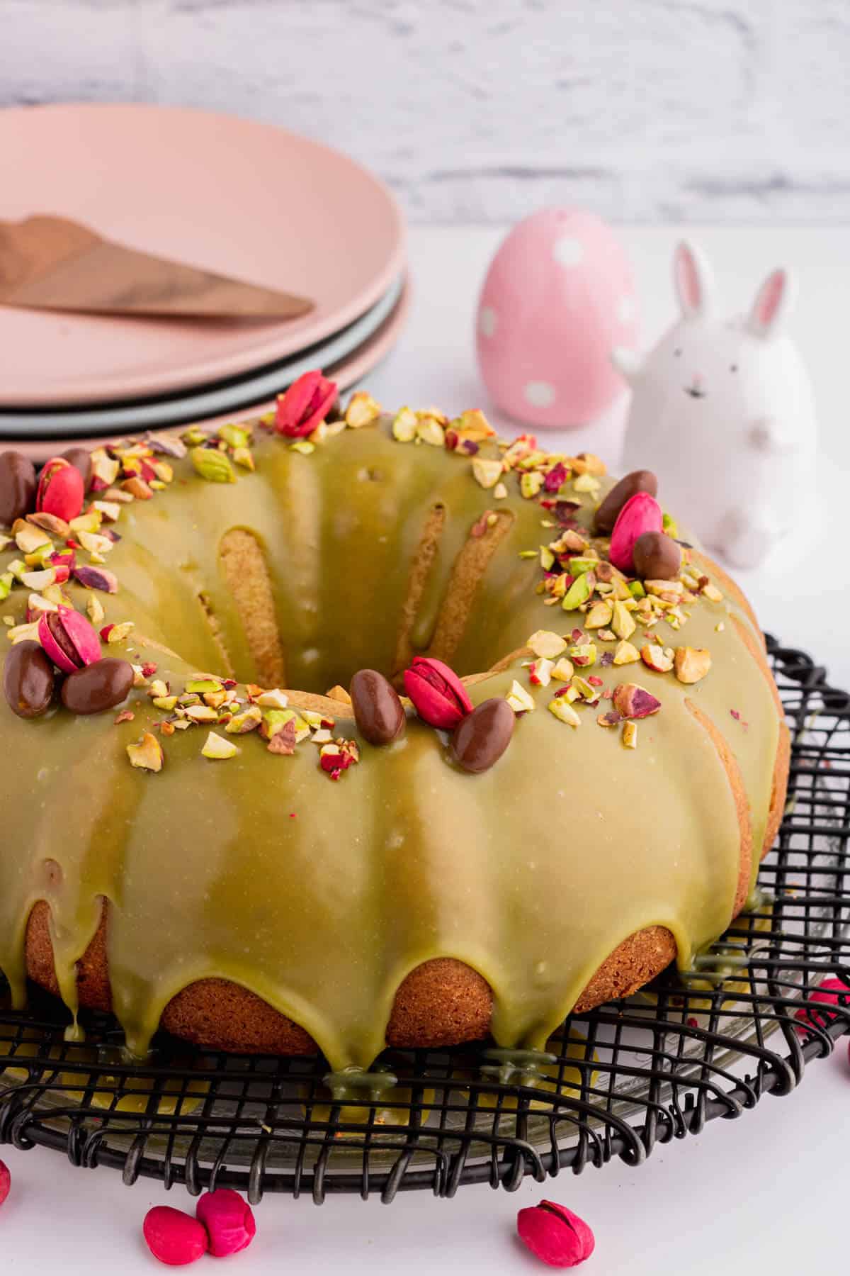 A green glazed bundt cake decorated with chopped pistachios, whole pink and chocolate pistachios. 