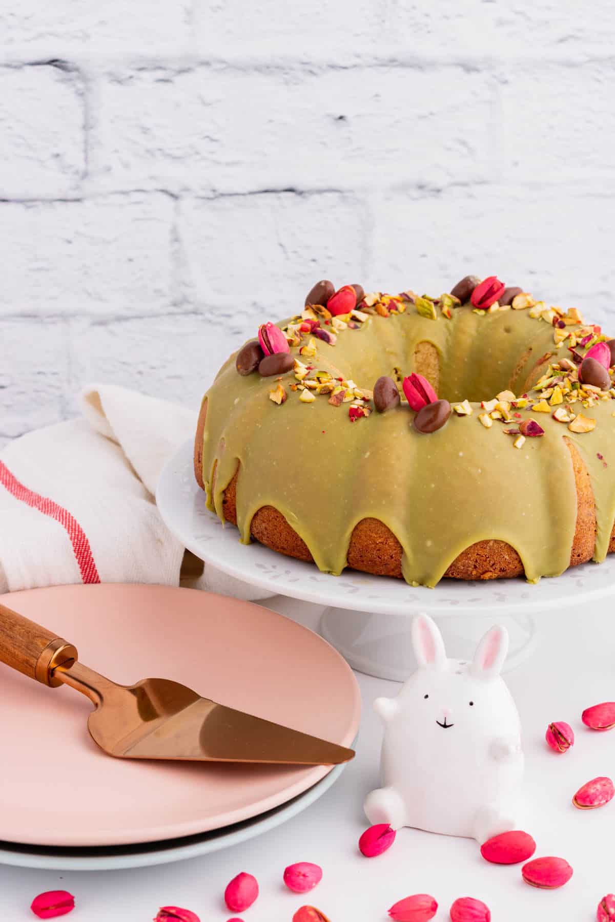 A green glazed bundt cake decorated with chopped pistachios, whole pink and chocolate pistachios.