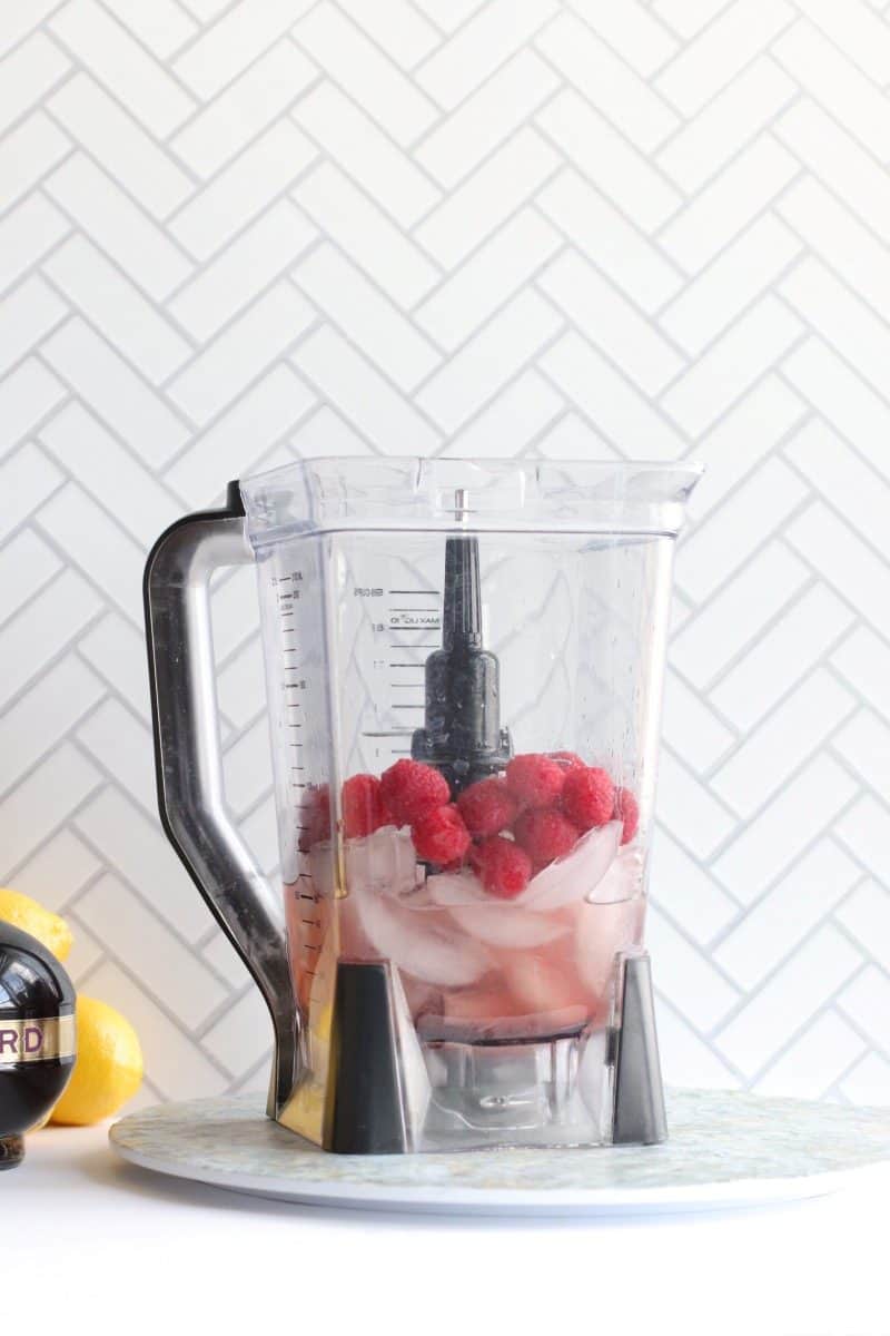 A blender with ice, liquor and raspberries
