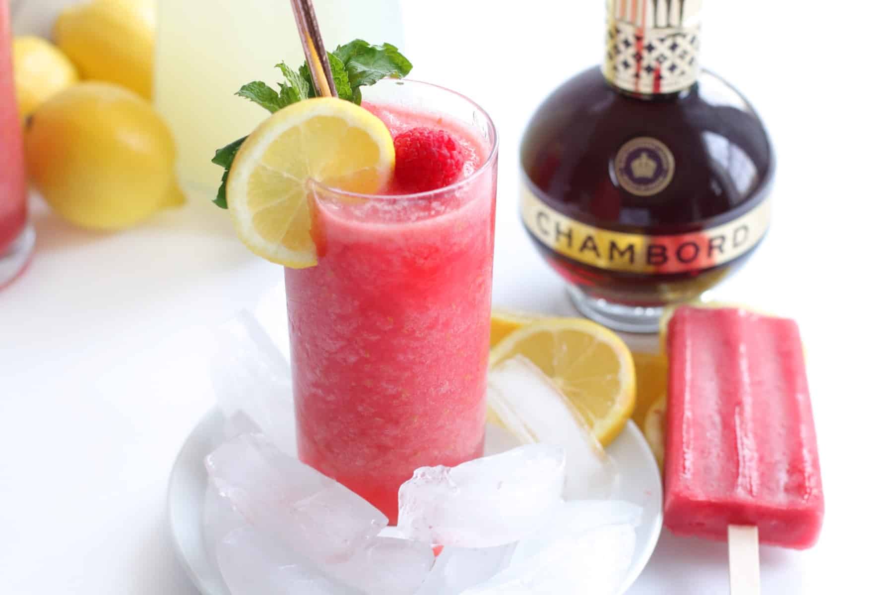 Showing a frozen lemonade in a tall glass with a bottle of Chambord and a raspberry popsicle