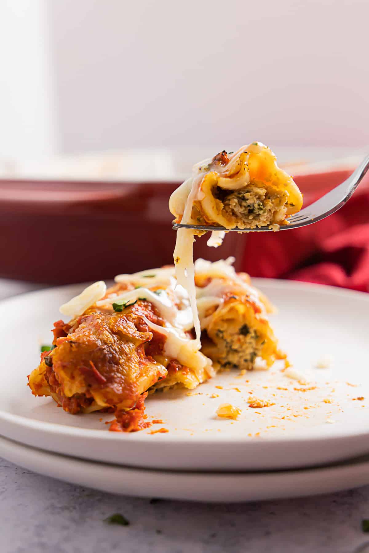 Side view of cheese manicotti on stacked white plates, a fork is pulling some cheese.